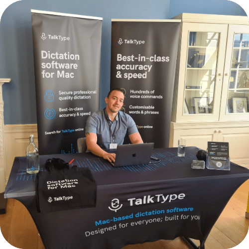 Stefano sitting at a TalkType stand at an event, smiling.