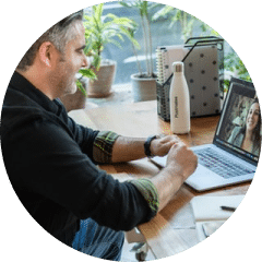 A middle aged man sitting at a table, smiling at his laptop.